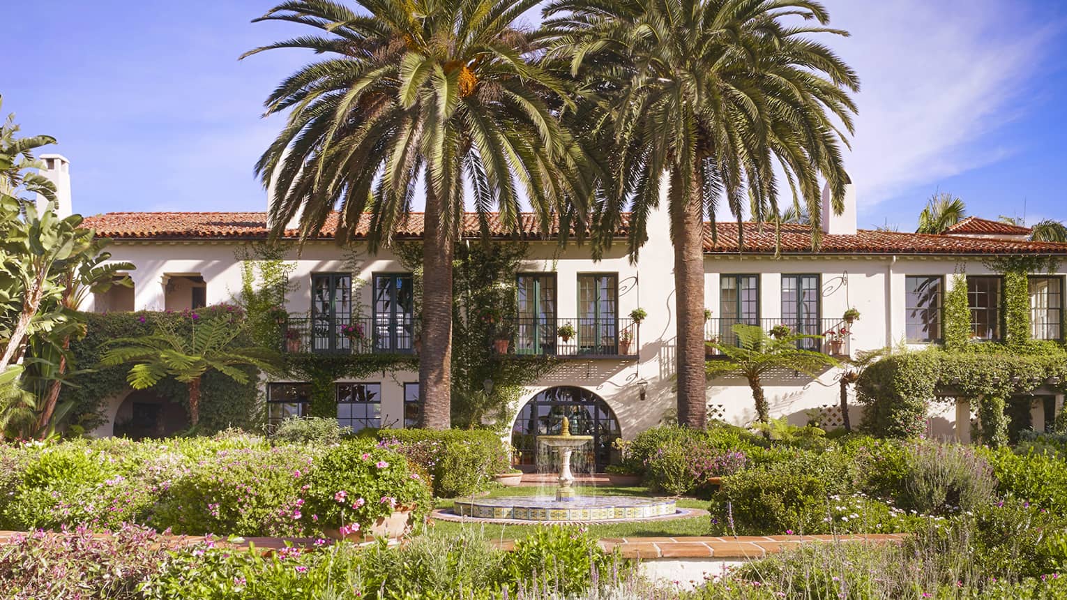 Fountain under palm trees in sunny garden in front of Four Seasons Hotel villa-style building