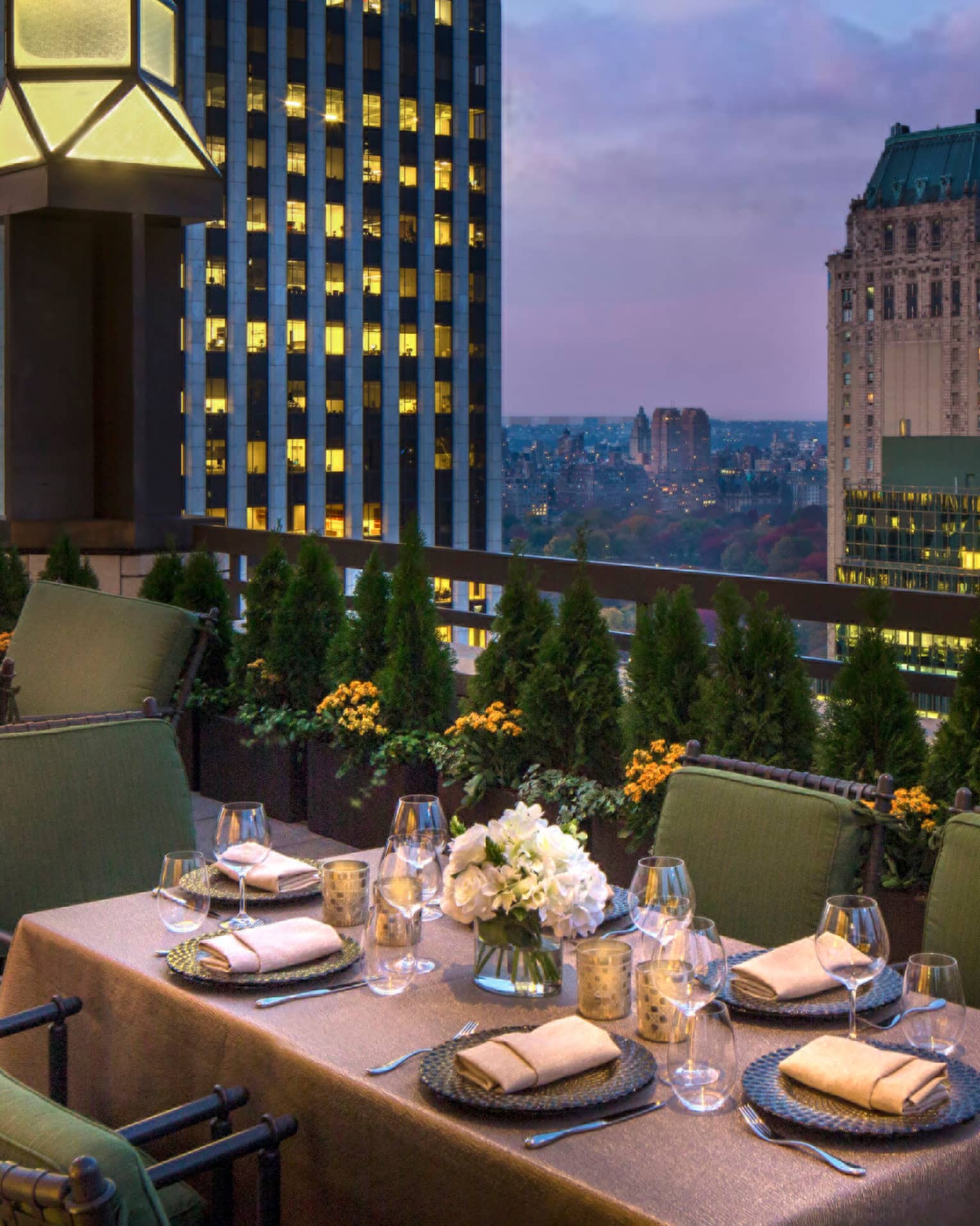 Private patio dining table with plush green cushions on chairs on rooftop terrace, city views at dusk