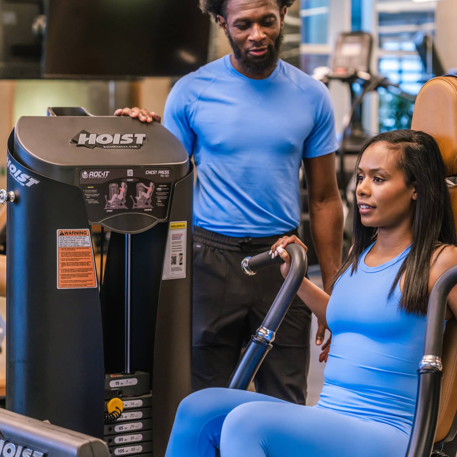 Two guests in a gym, one guest using a gym machine.