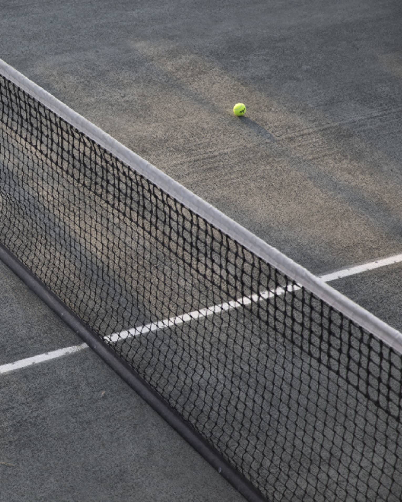 A lone tennis ball lies near the net on an empty court