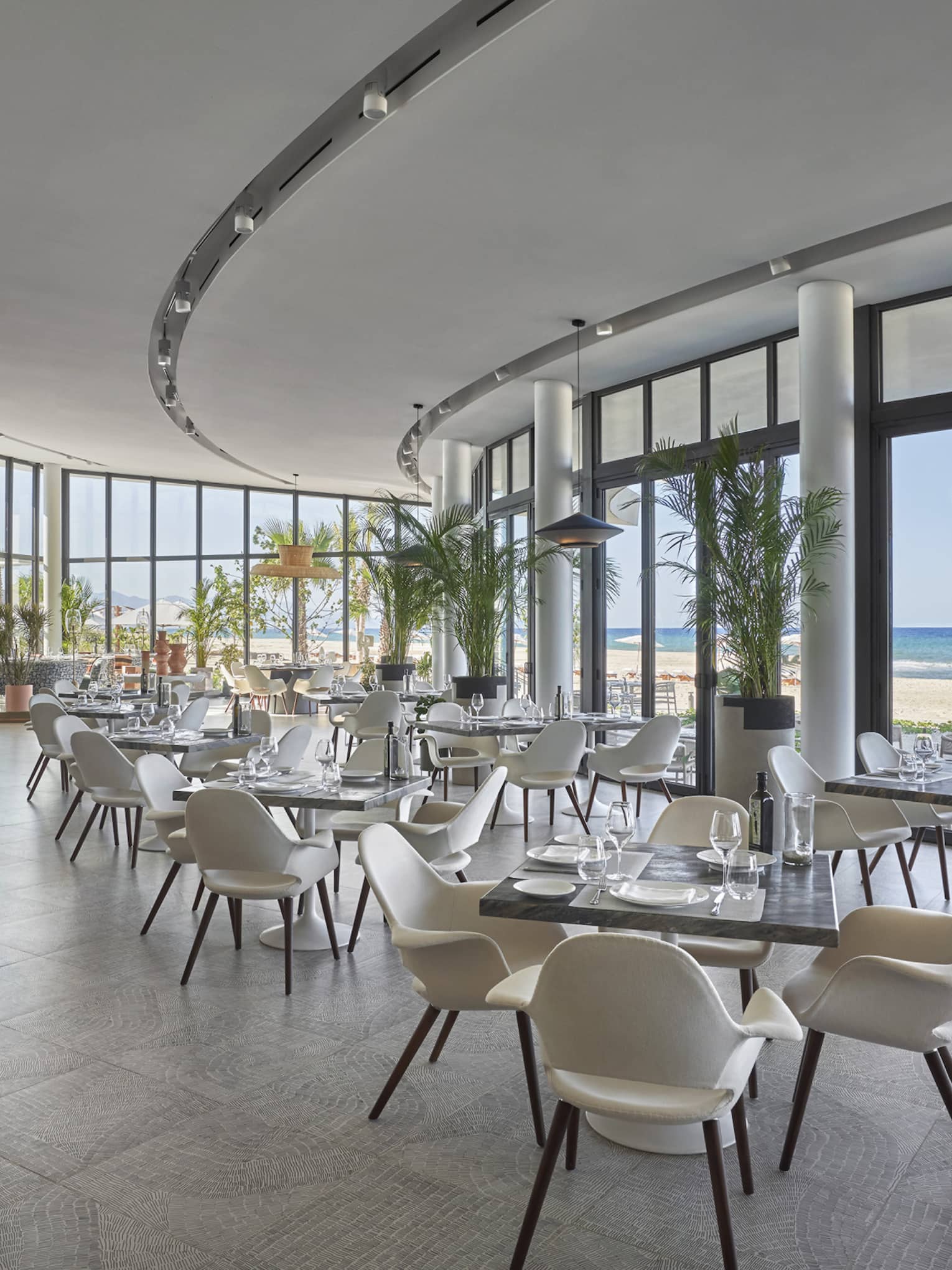 Milos contemporary curved dining room with square tables and white chairs, water views