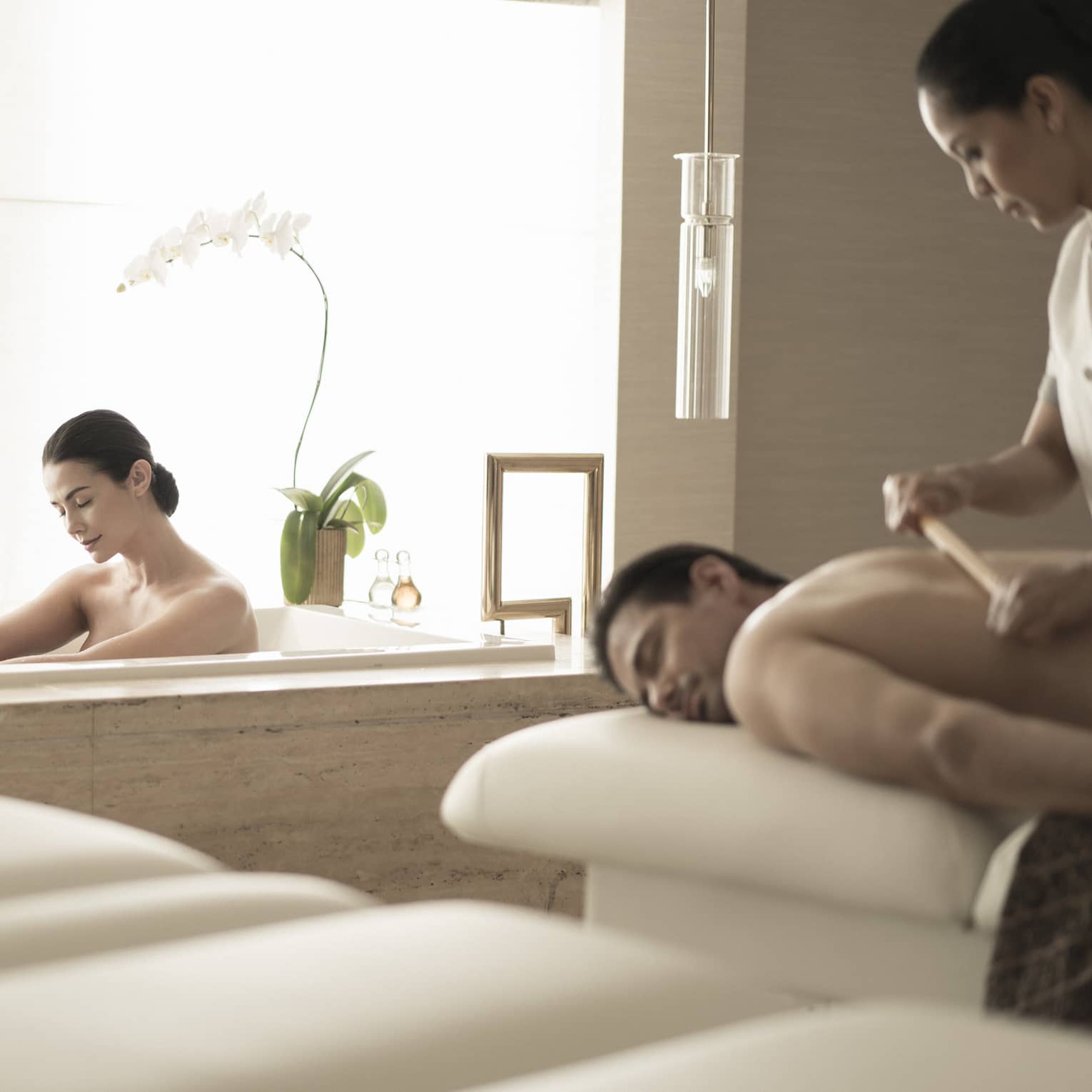 Woman soaks in spa tub near man getting massage 