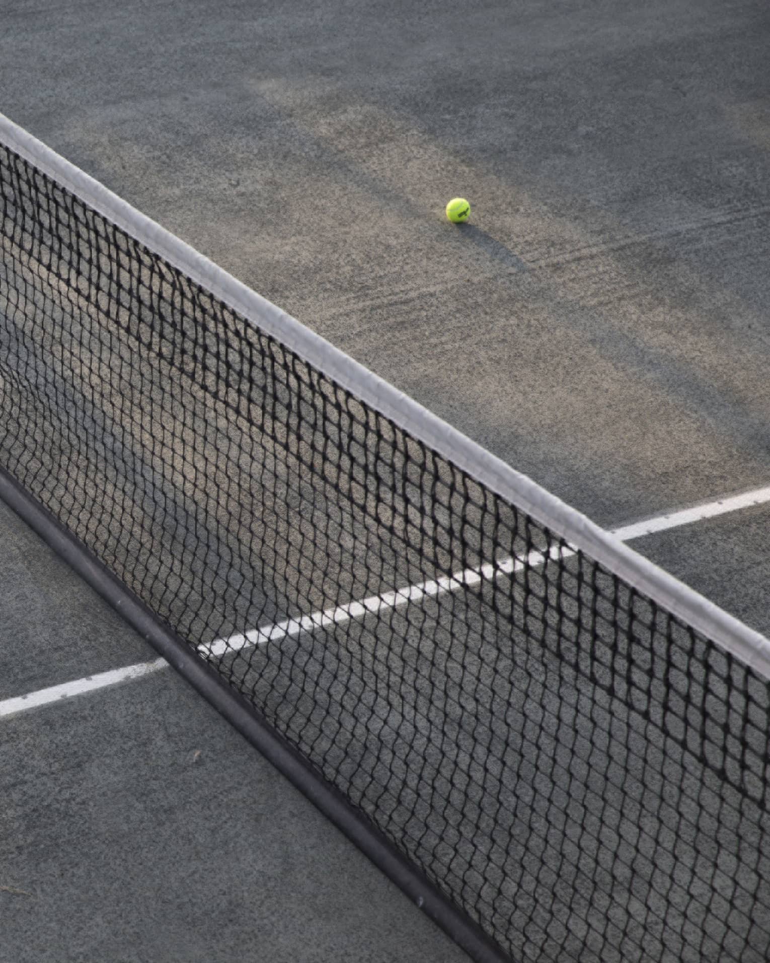 A lone tennis ball lies near the net on an empty court