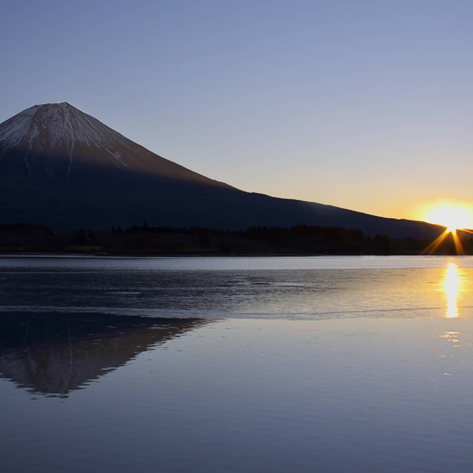 Sun rising behind a mountain with a reflection on a calm lake