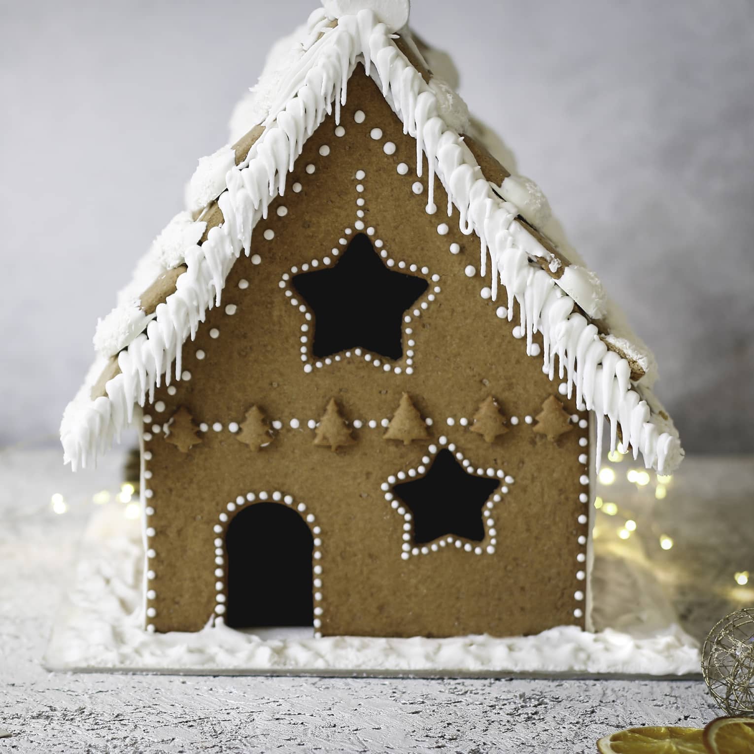 Gingerbread house decorated with white icing amid white background and white lights