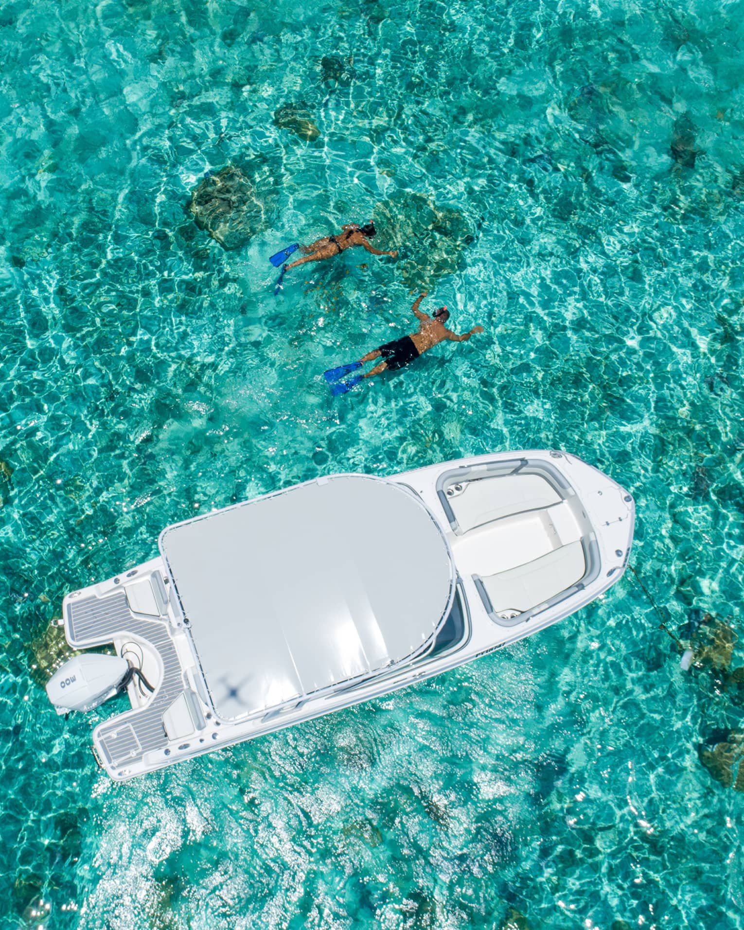 Two people swim alongside a boat in clear turquoise waters