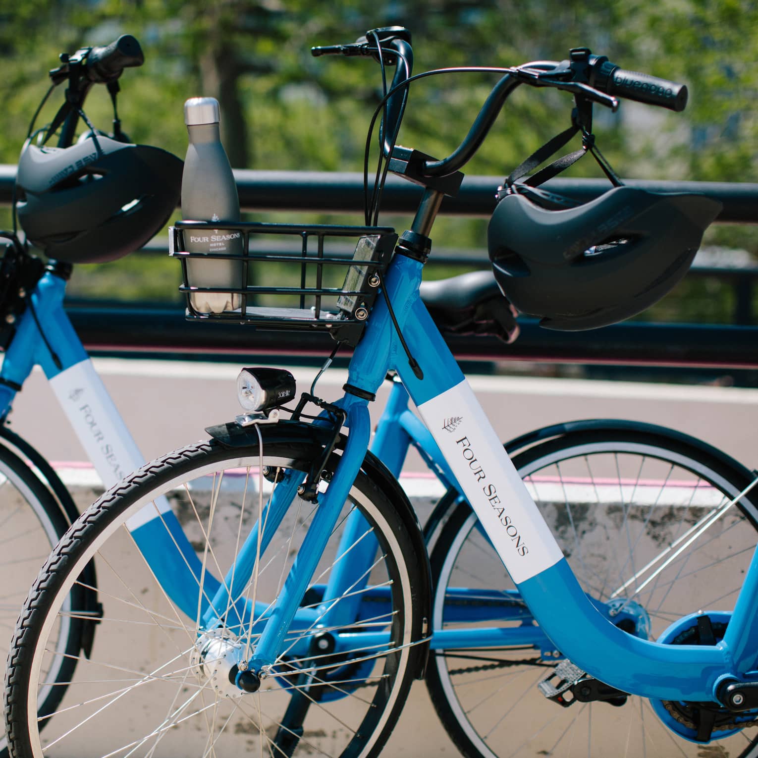 Close-up of two blue Four Seasons bicycles with helmets hanging on the handlebars and a water bottle in one bicycle's basket.