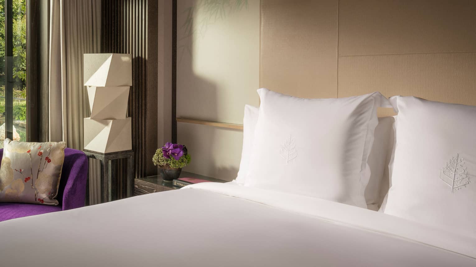 Four Seasons Executive Suite bed by bright purple armchair, modern white lantern by glass door