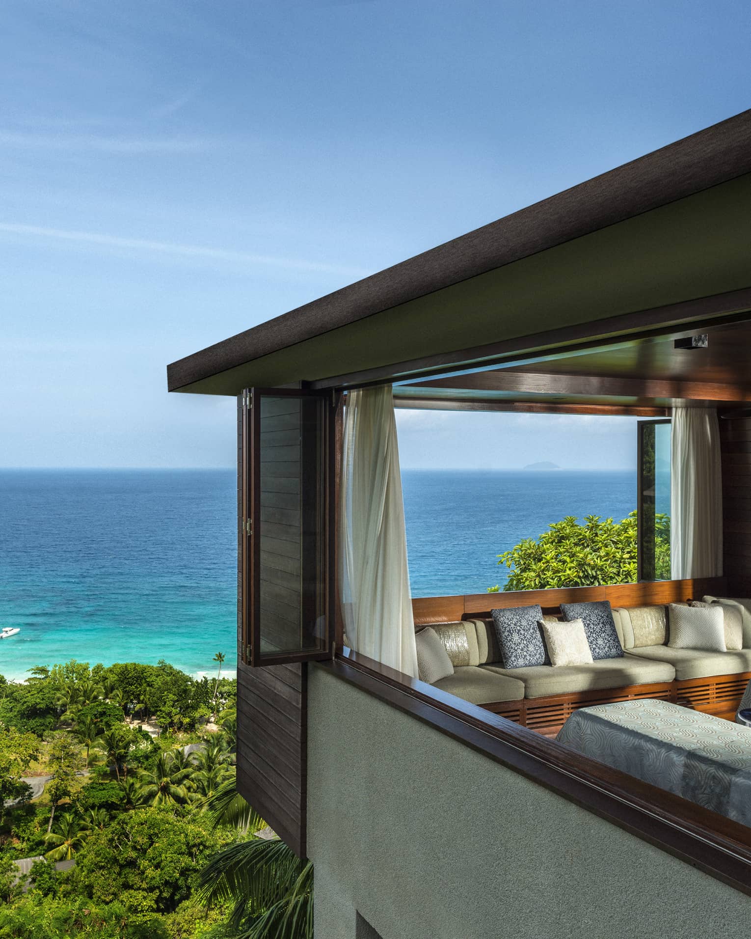 Two side-by-side massage tables in spa room high above trees, ocean