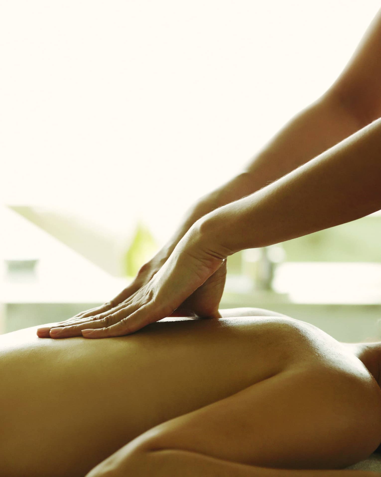Masseuse reaches over, massages woman's bare back as she lies on spa table
