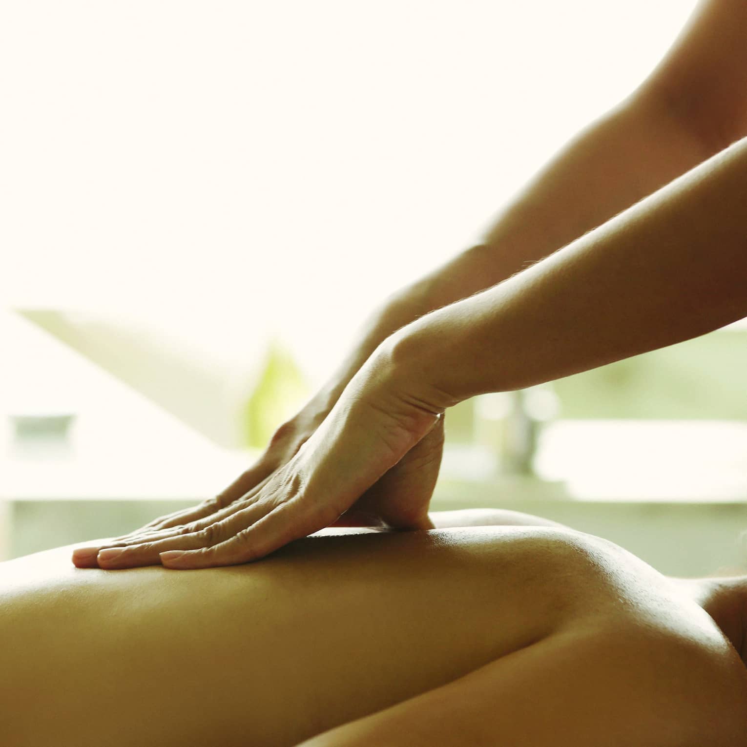 Masseuse reaches over, massages woman's bare back as she lies on spa table