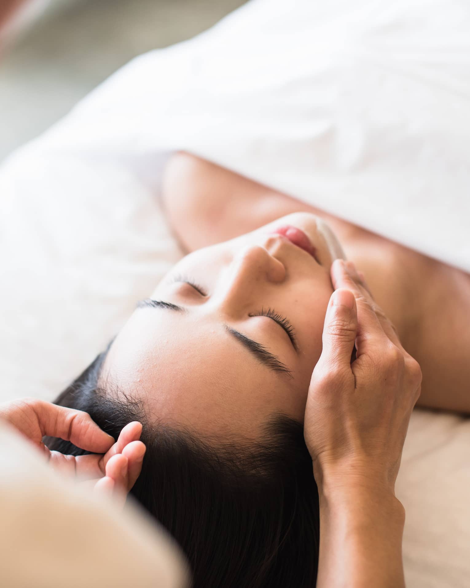 A guest receiving a soothing facial at a spa, lying on a massage table, surrounded by calming décor and soft lighting.