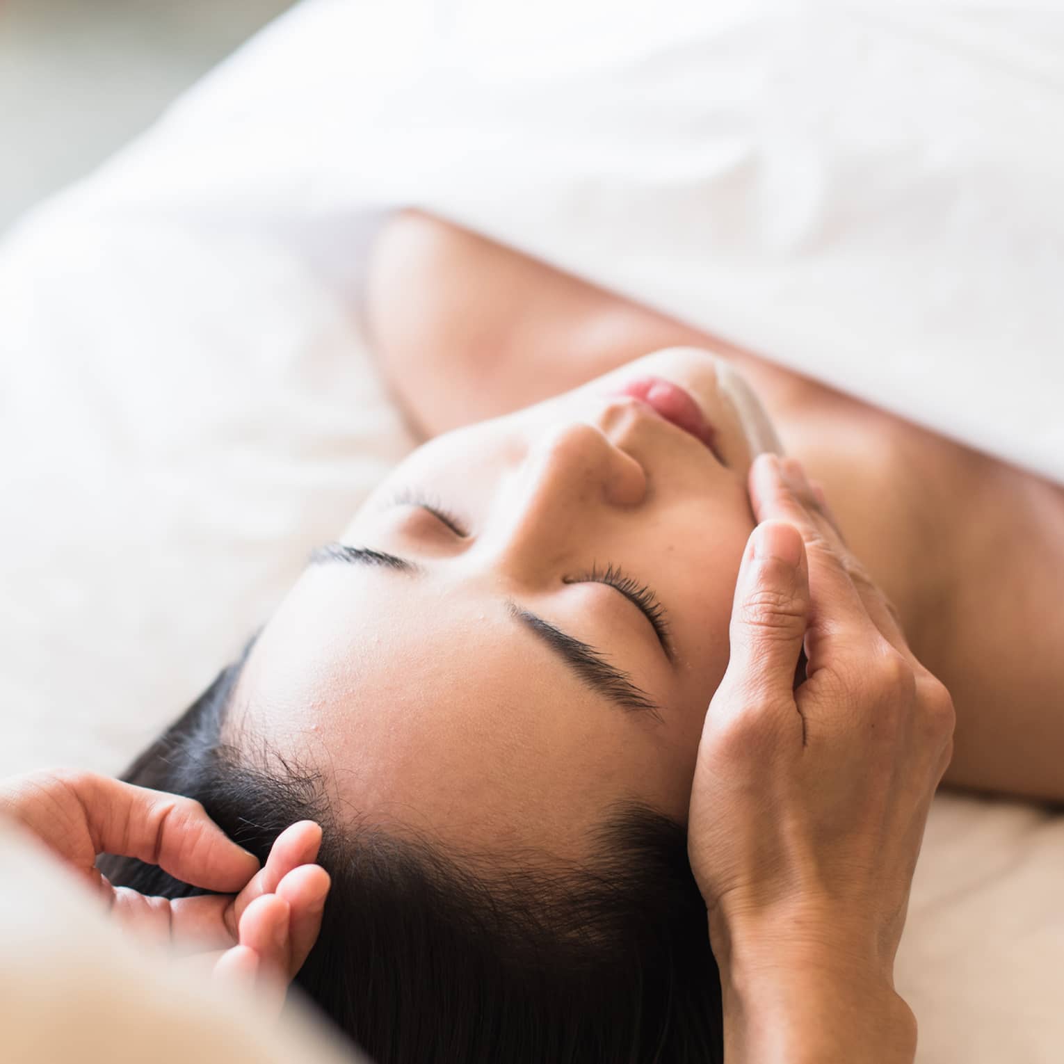 A guest receiving a soothing facial at a spa, lying on a massage table, surrounded by calming décor and soft lighting.