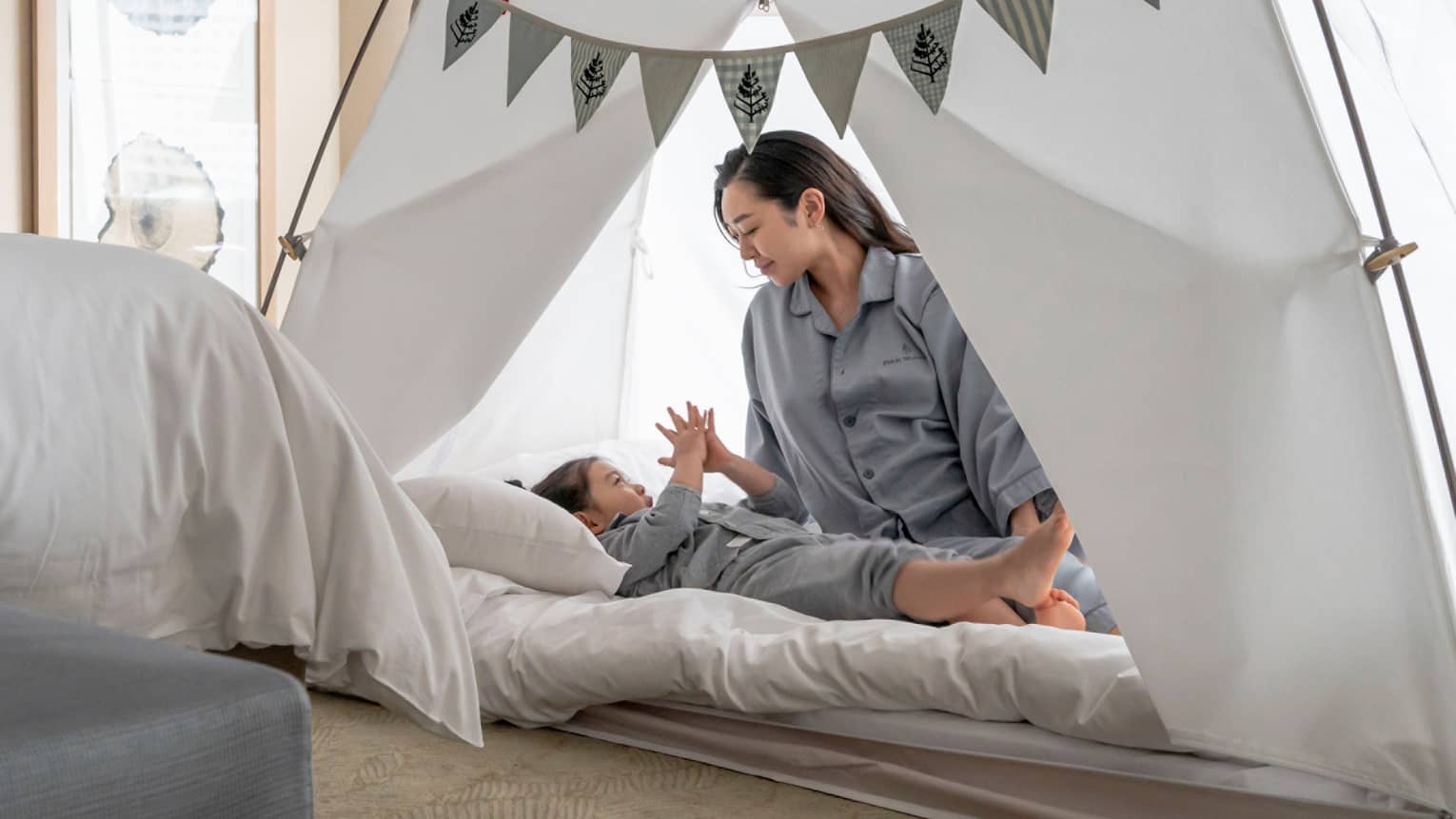 Parent and child in pyjamas playing together inside a cozy tent with bunting decorations