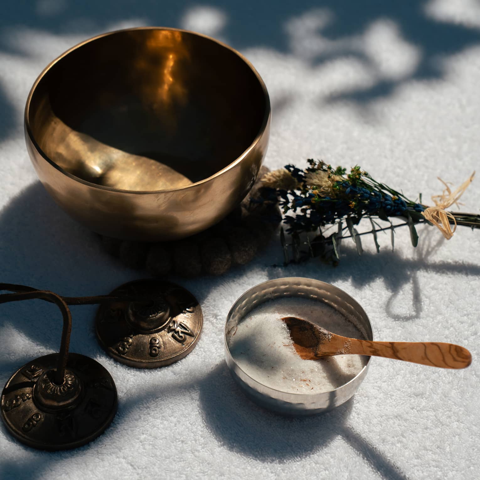 A small empty metal bowl, a small bundle of plants, a small bowl containing a whitish substance and a small spoon, and a set of small metal bells.