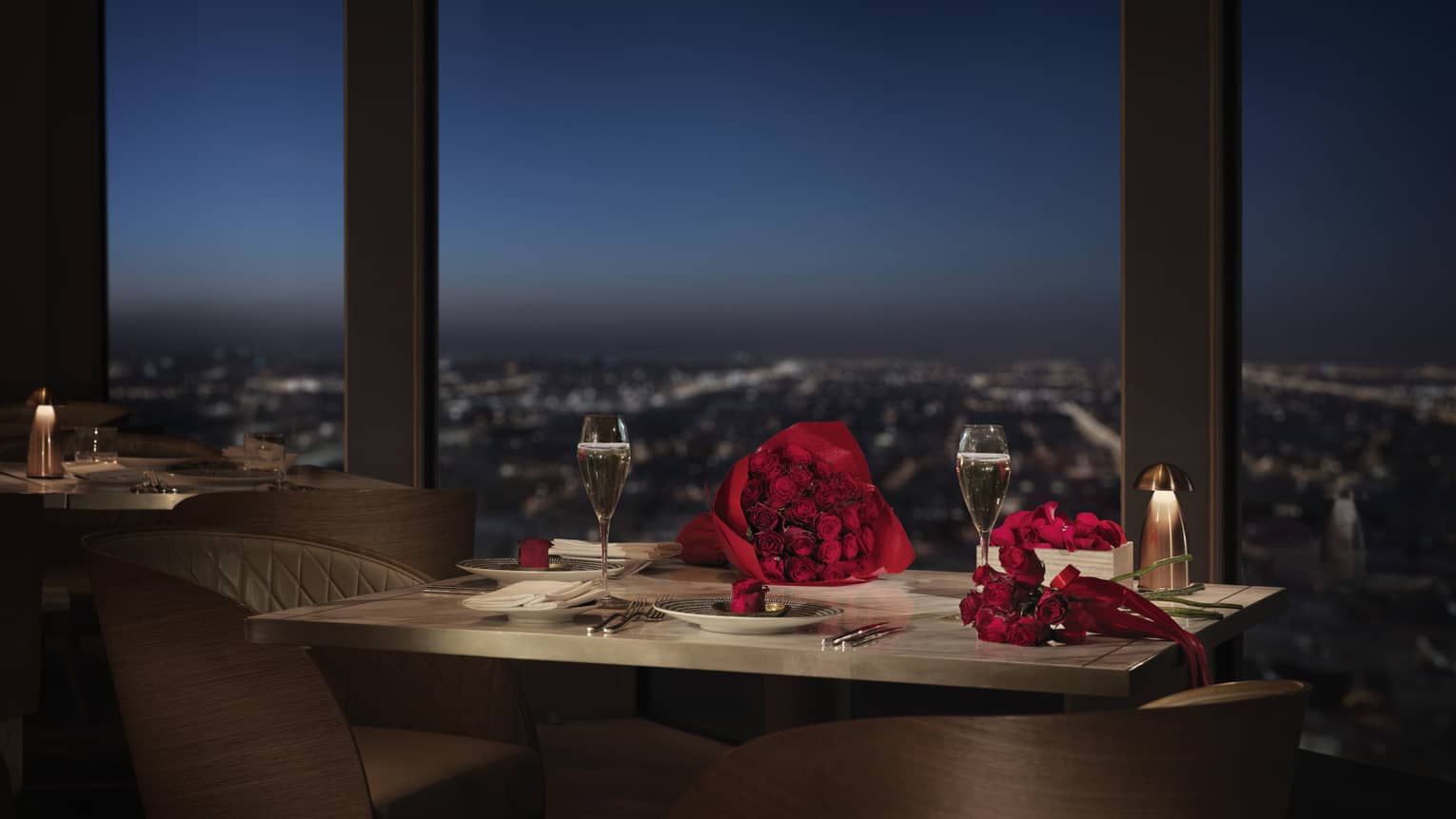 Red roses on small dining table by window overlooking city lights below