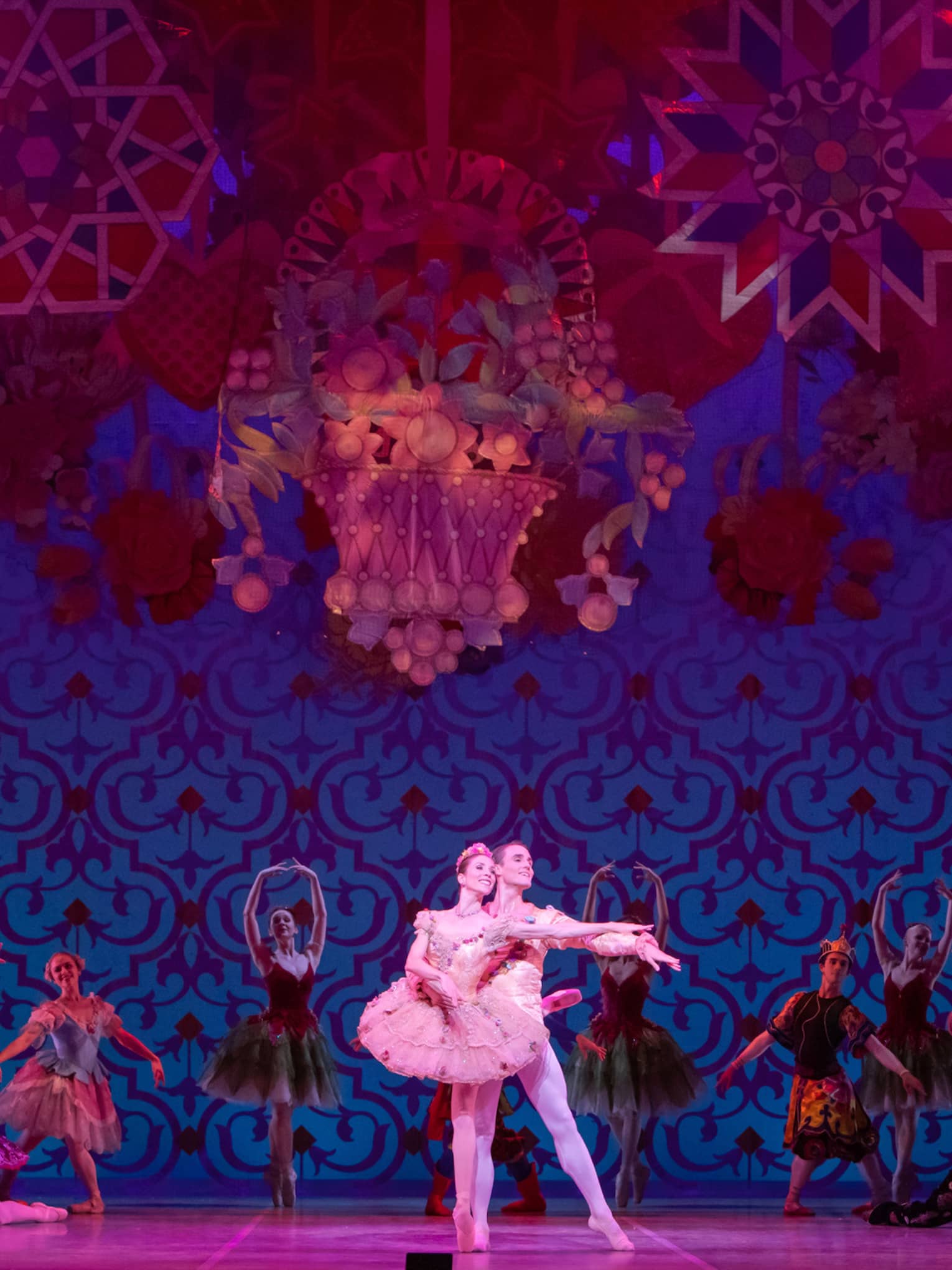 Two dancers performing ballet with back up dancers behind them in a red and blue scene.