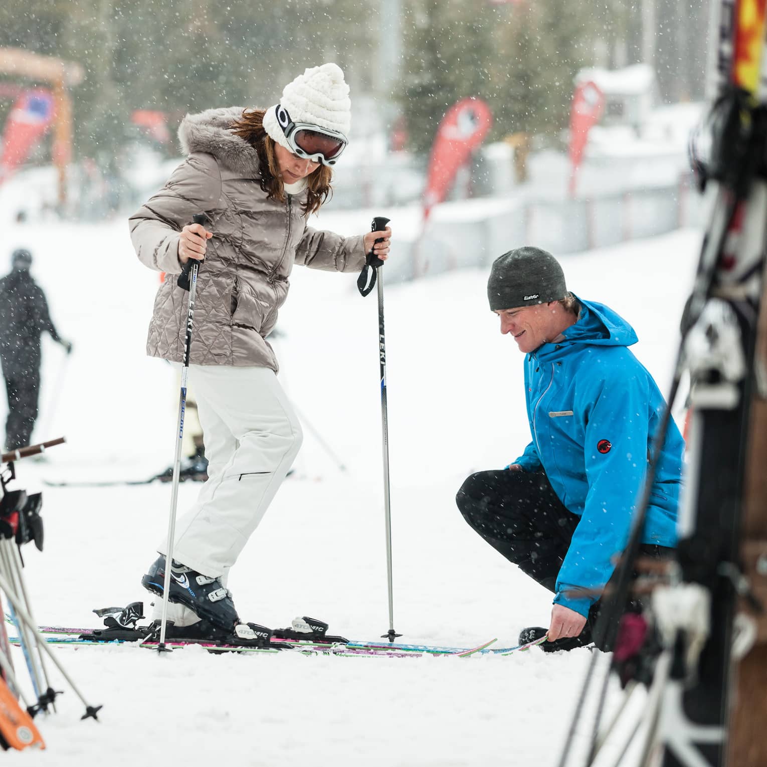 Ski concierge kneels down by woman trying on skis in front of rack