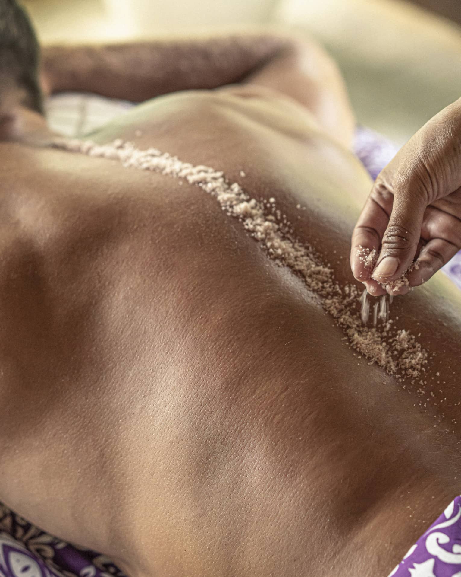 Hand place spa salts along man's spice during Sacred River Spa Massage