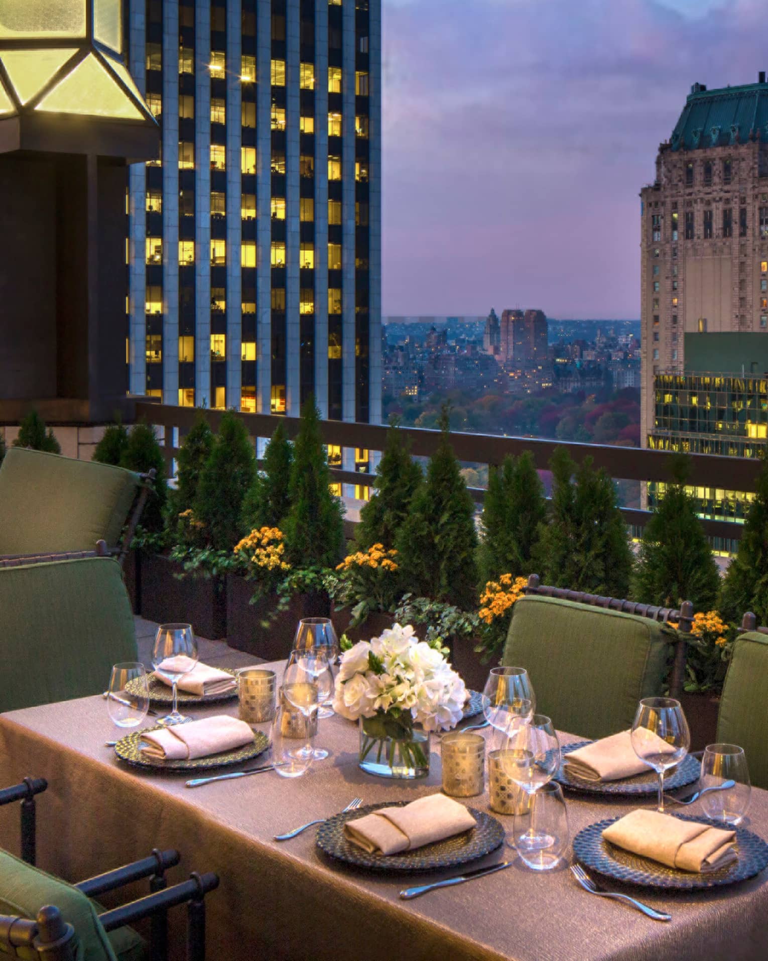 Private patio dining table with plush green cushions on chairs on rooftop terrace, city views at dusk