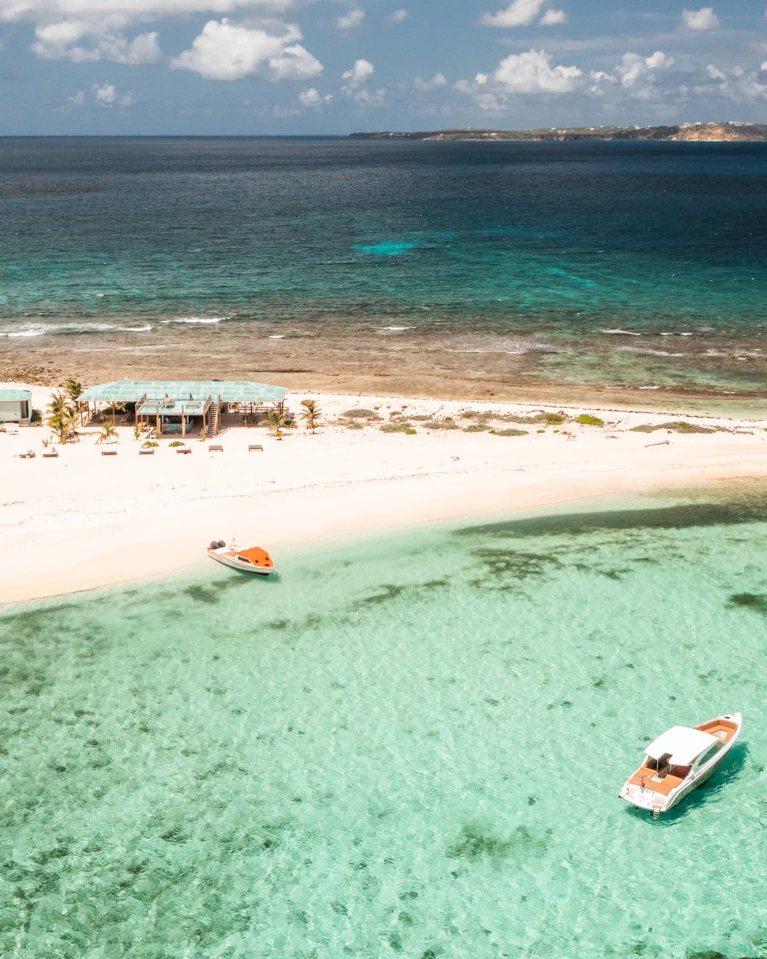 A small sandy island surrounded by crystal clear water and a few boats