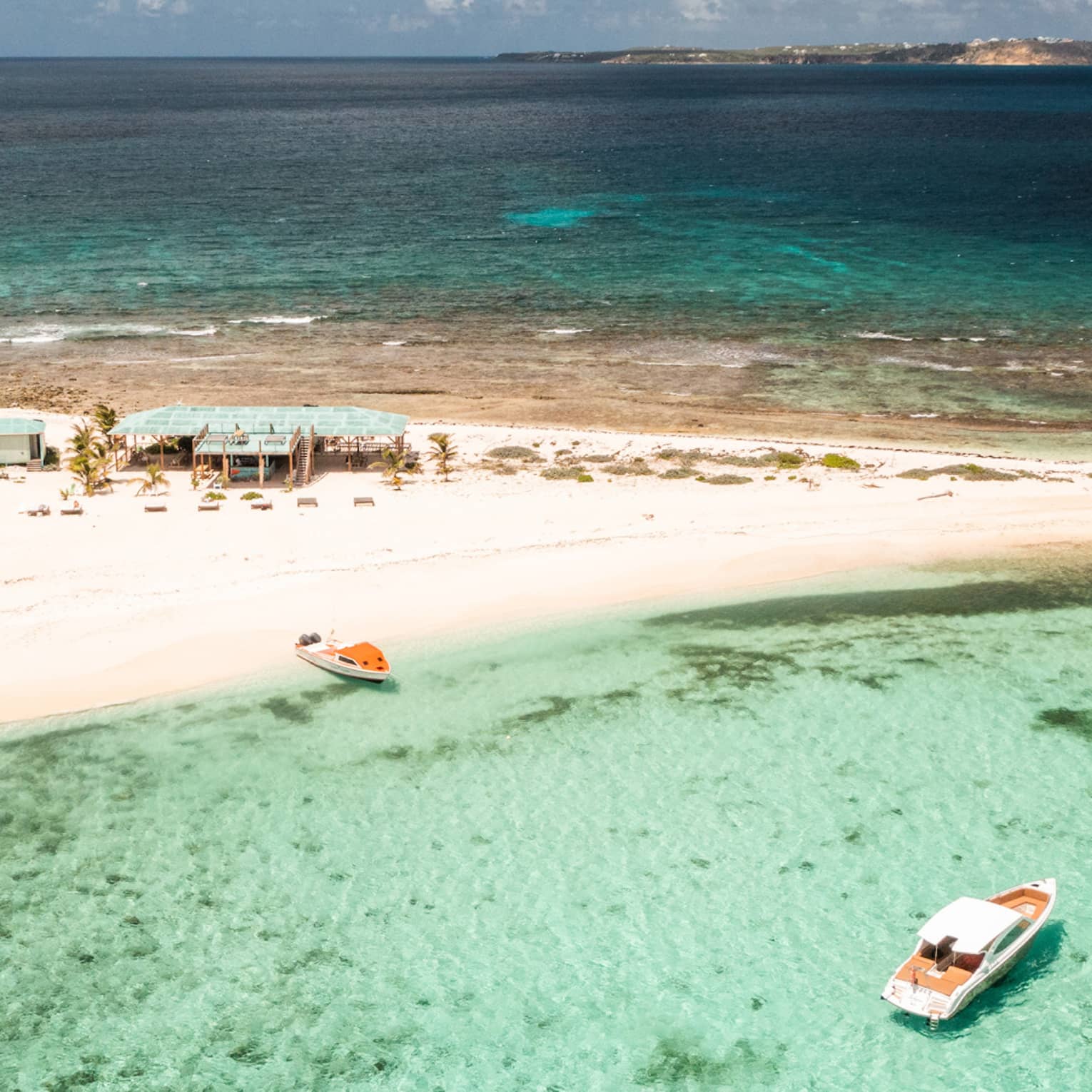 A small sandy island surrounded by crystal clear water and a few boats