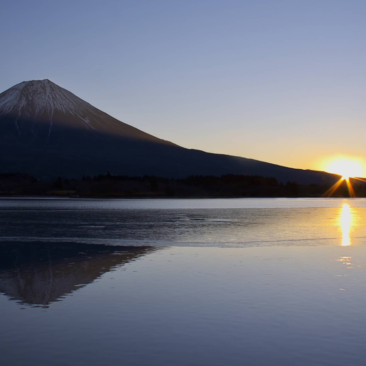 Sun rising behind a mountain with a reflection on a calm lake