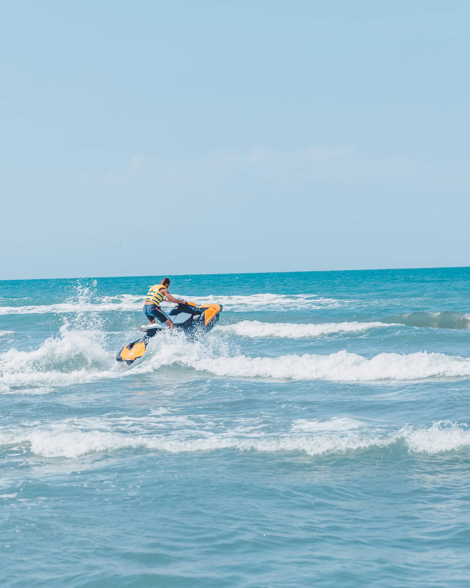 Person riding jet ski along waves in blue ocean