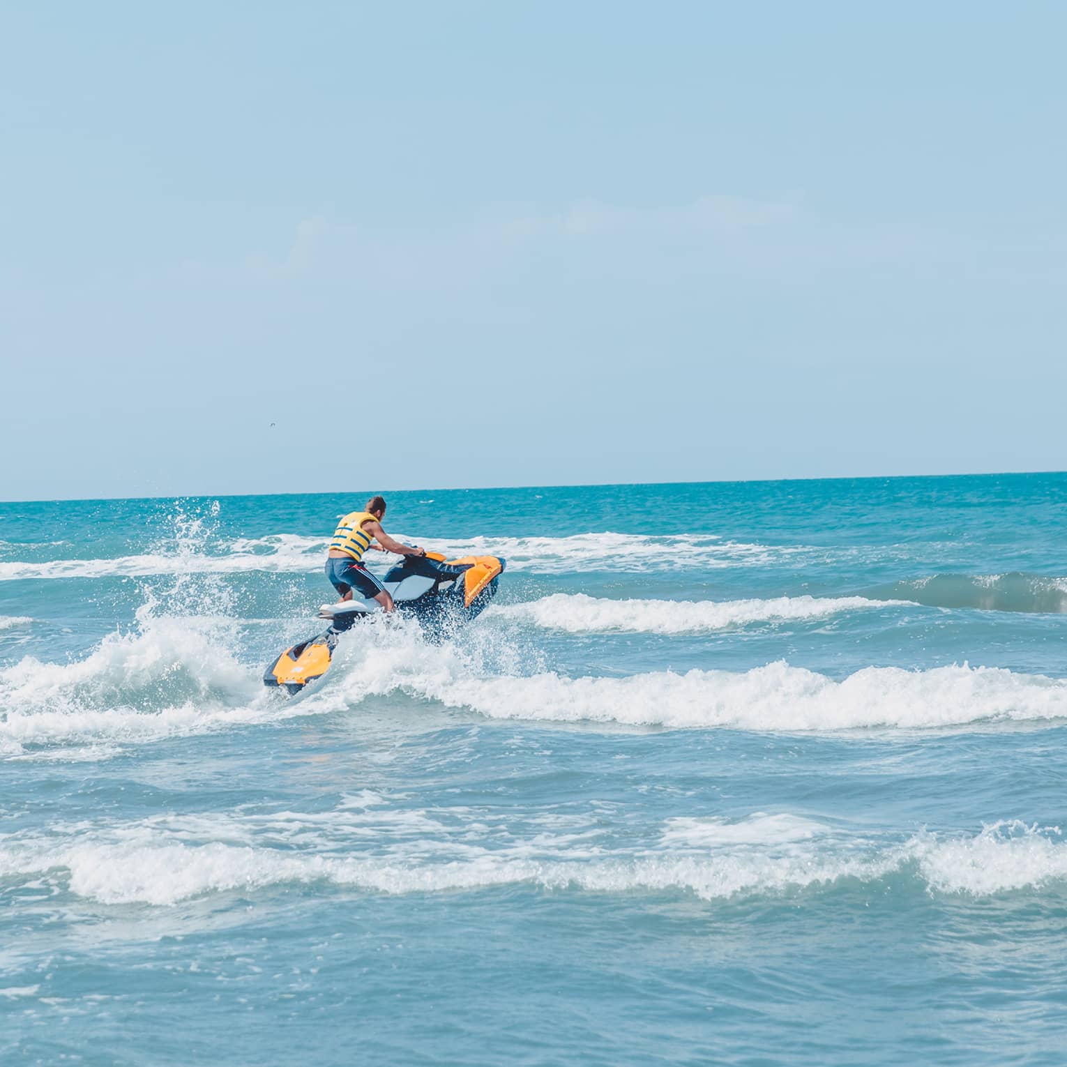 Person riding jet ski along waves in blue ocean