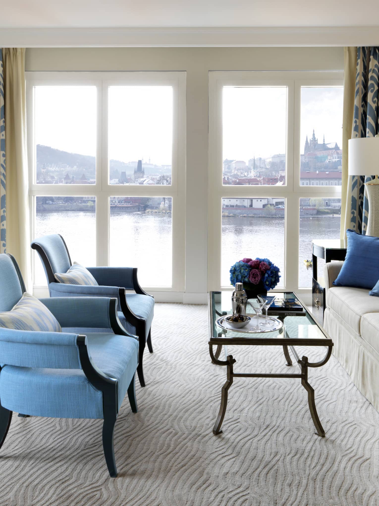 River Suite with two blue armchairs in front of glass coffee table, sofa, floor-to-ceiling windows with Vltava River view