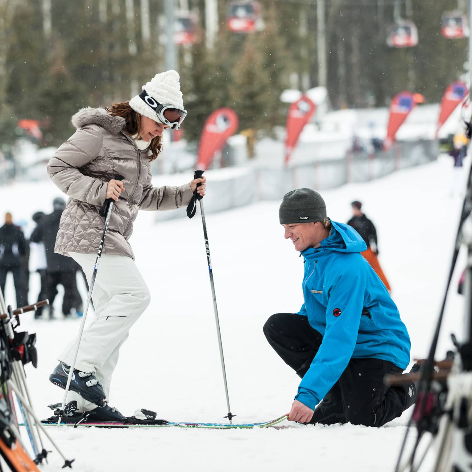Hotel staff holds skis as woman holding poles steps in by ski rack, snowy hill