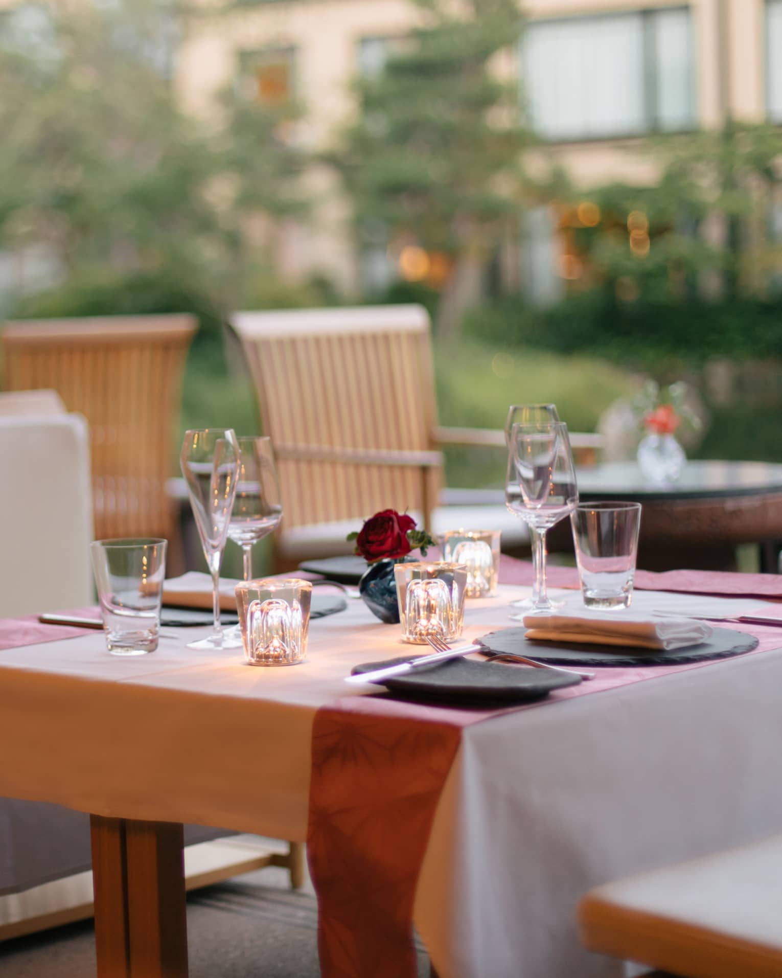 Elegant outdoor dining table set with wine glasses, a small red rose centerpiece and soft lighting at Four Seasons 