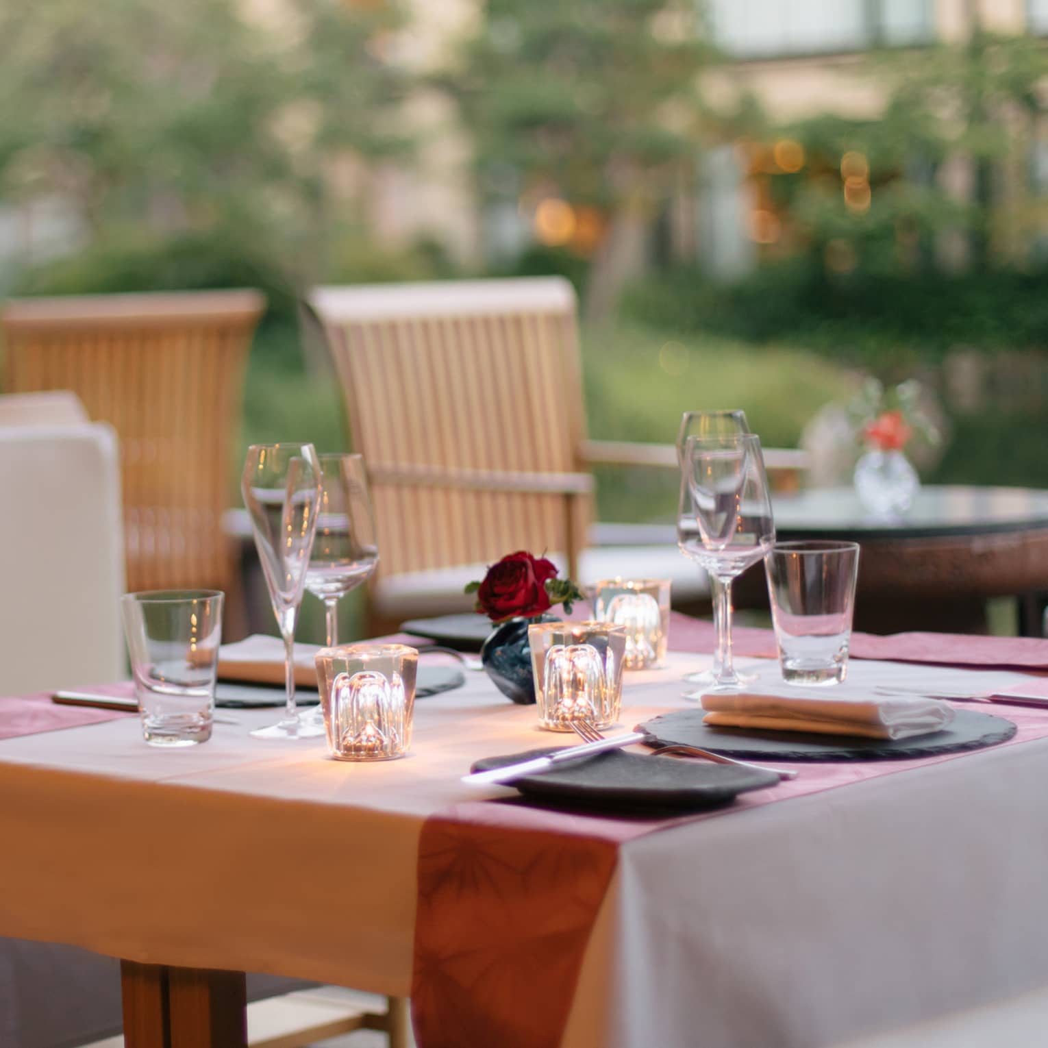Elegant outdoor dining table set with wine glasses, a small red rose centerpiece and soft lighting at Four Seasons 