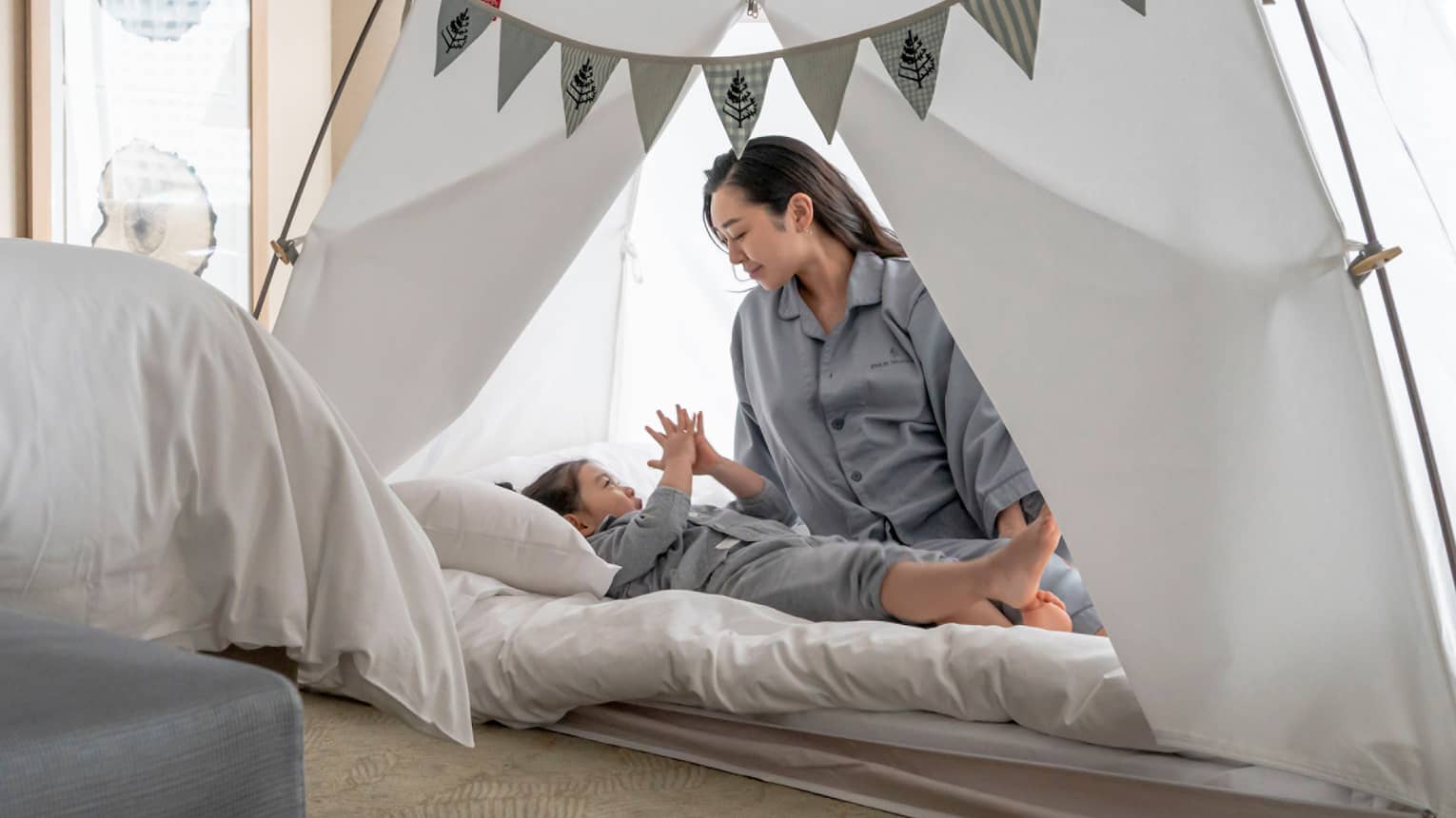 Parent and child in pyjamas playing together inside a cozy tent with bunting decorations