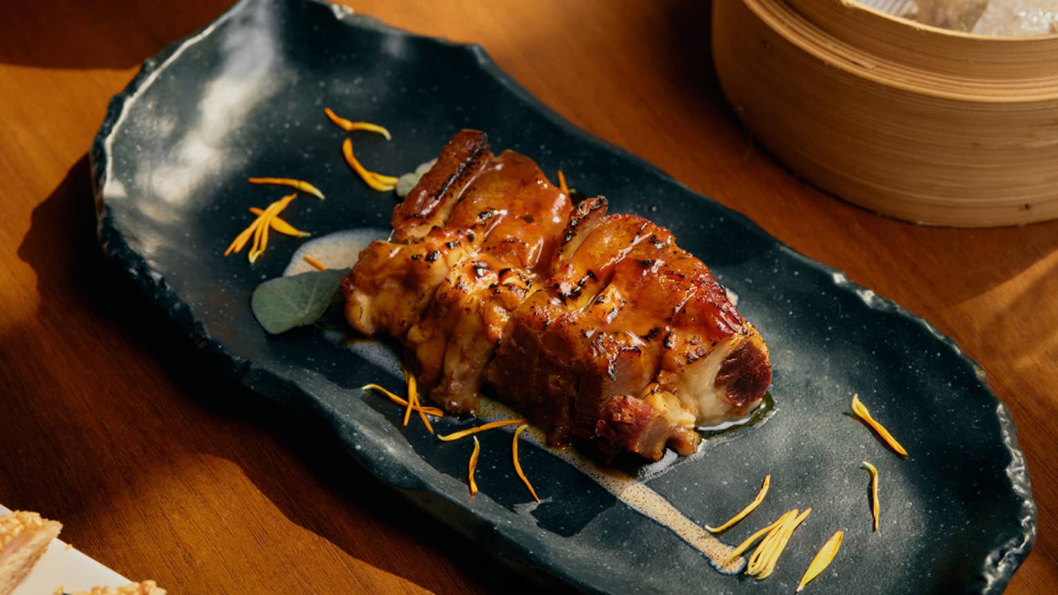 An oblong, artistic black serving plate holds roasted meat with garnishes.