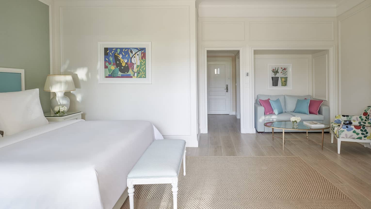 White room, white bed with blue headboard on green wall, foot bench, wood floor, seating area
