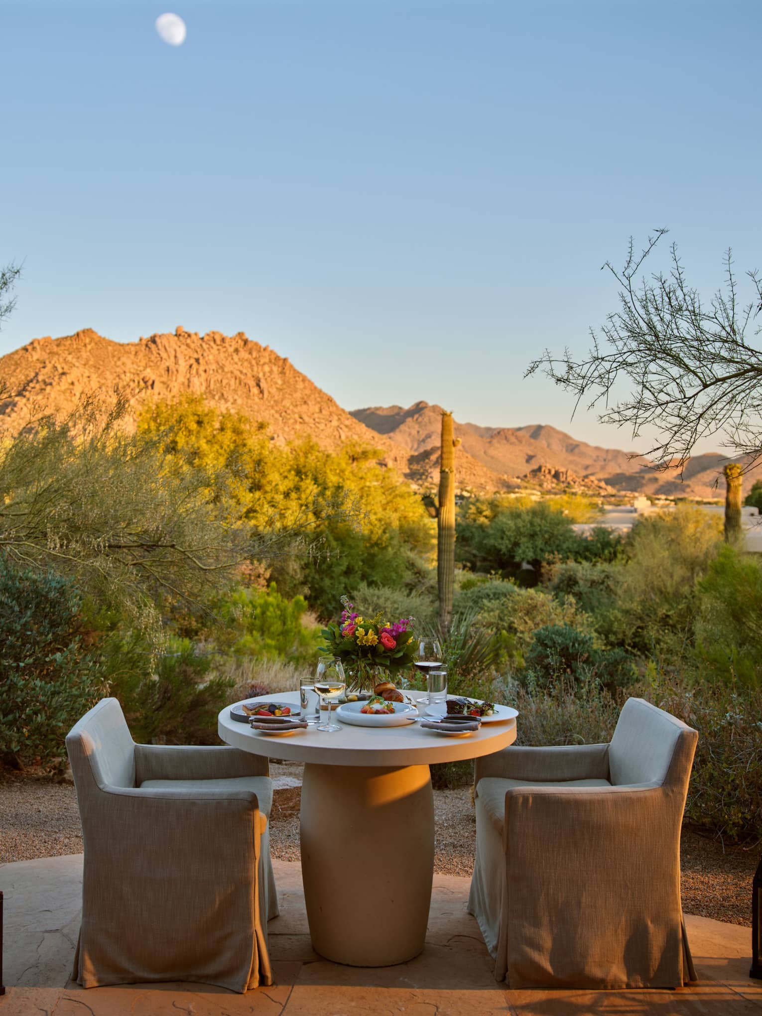 Two chairs and a table outside with lanterns and a view of the mountains.
