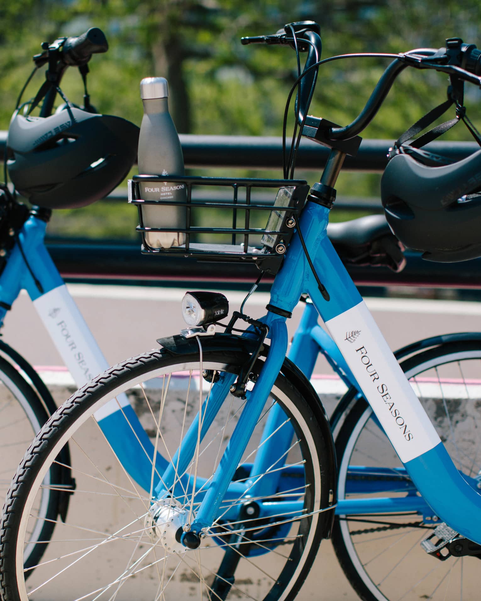 Close-up of two blue Four Seasons bicycles with helmets hanging on the handlebars and a water bottle in one bicycle's basket.