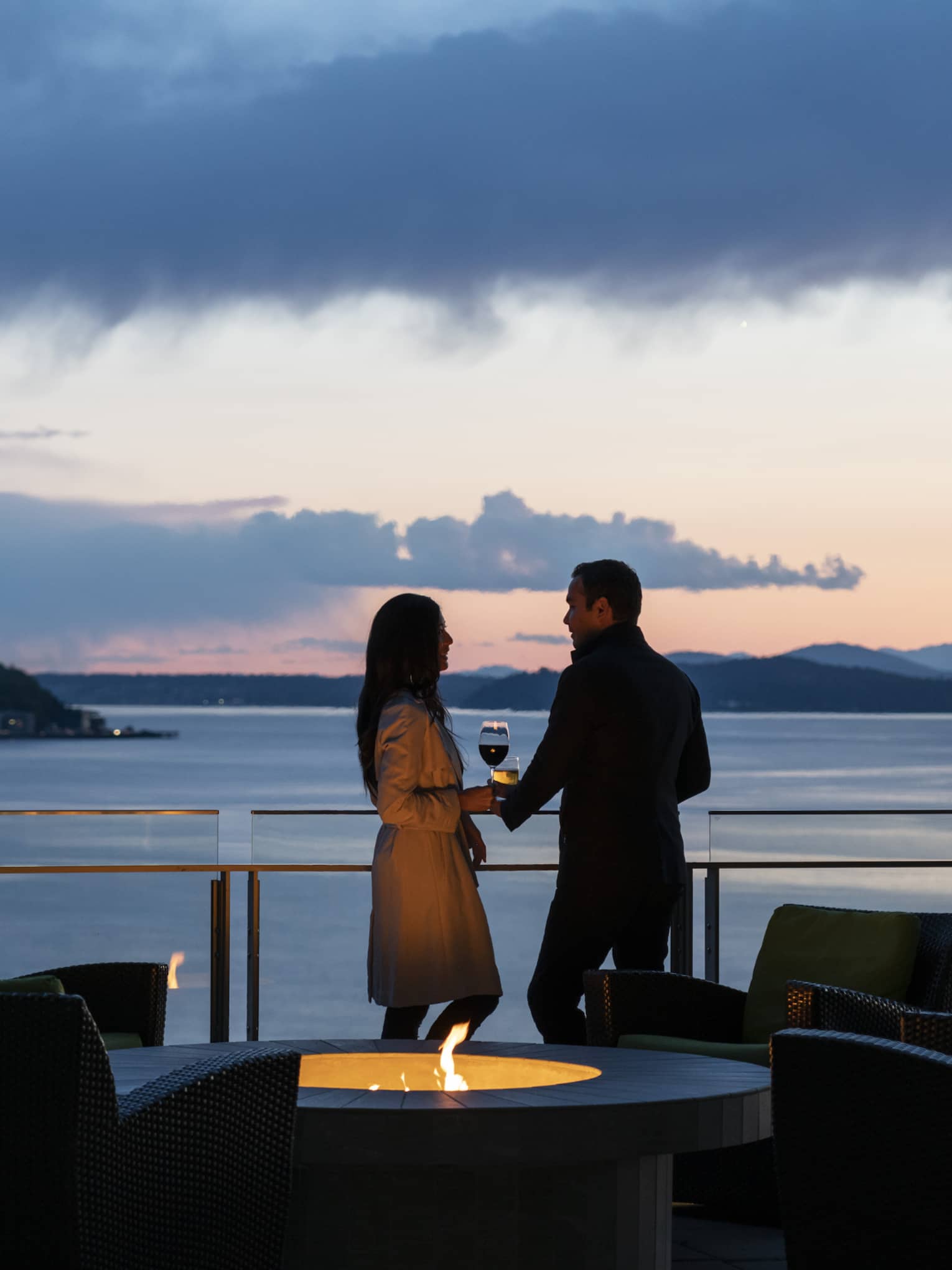 A couple holds hands and shares wine on the balcony as the sun sets