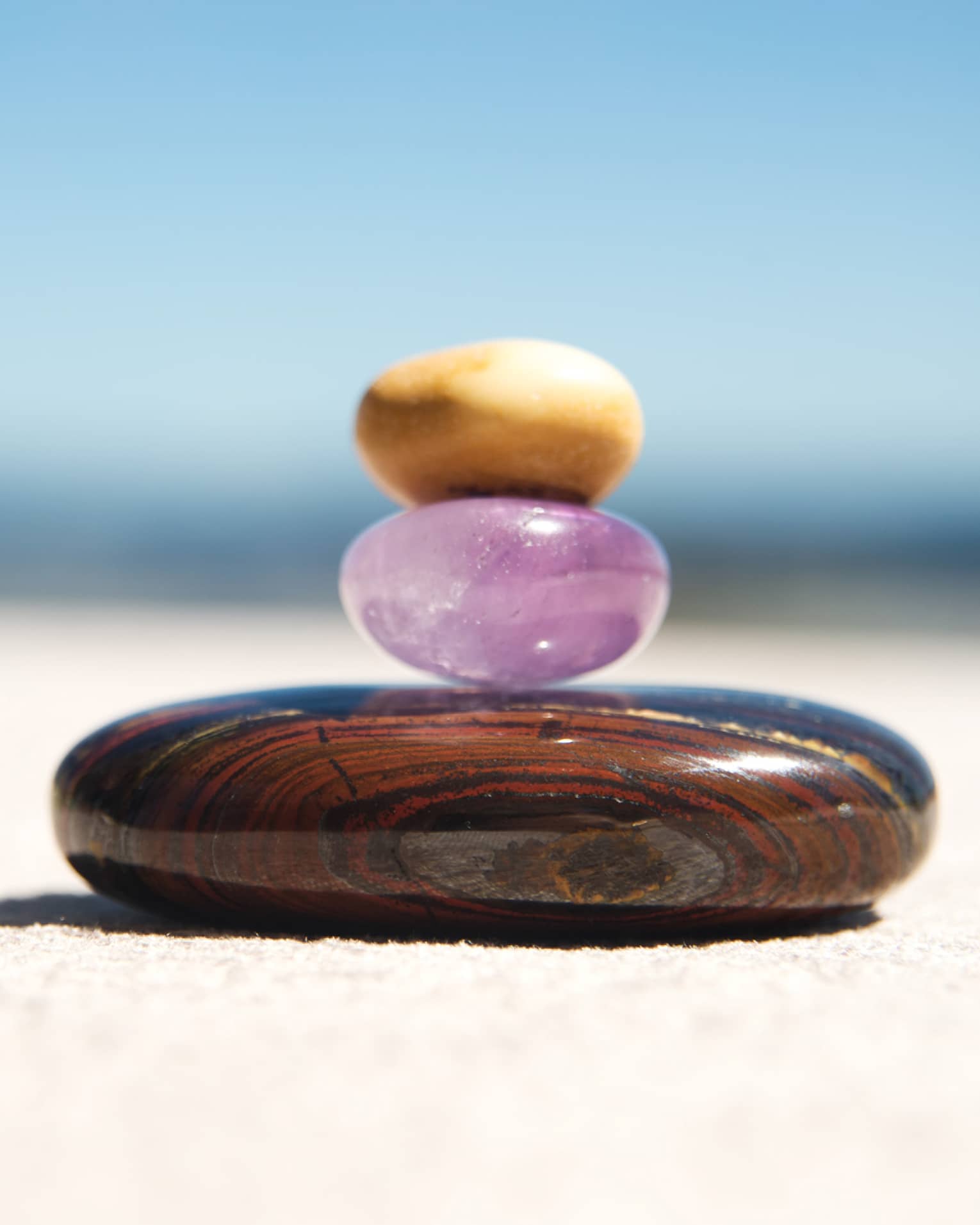 A small round amythest and a small round yellow crystal are stacked on top of a larger round, brown stone