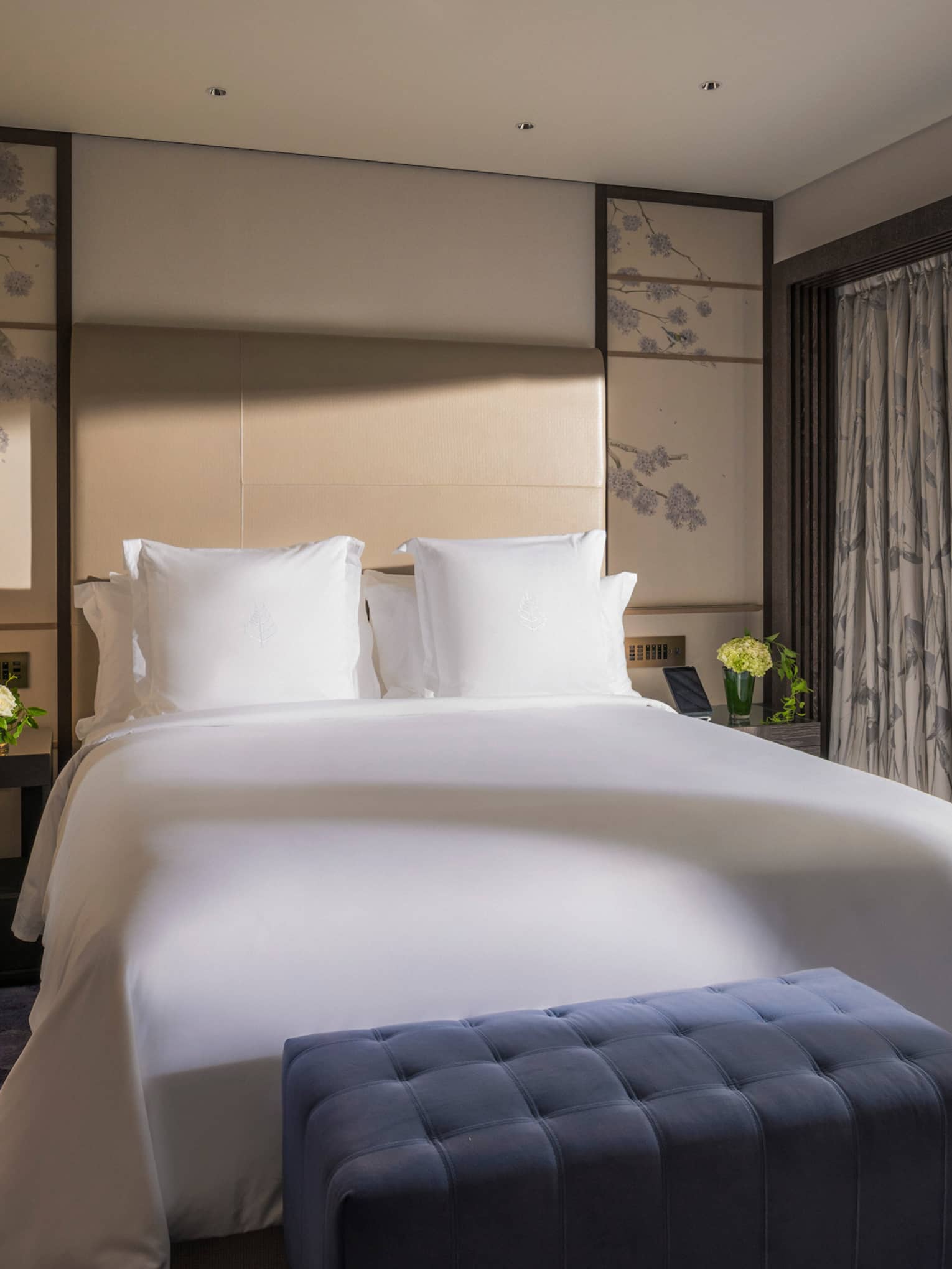 Bright bedroom with a king-size bed, a blue tufted bench and sliding glass doors opening to a private terrace with garden view