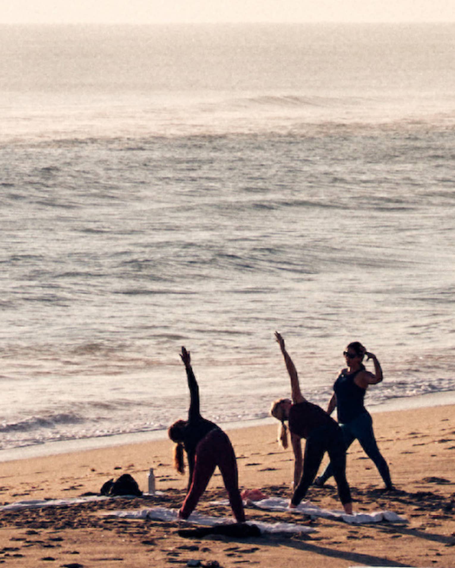 Three guests doing yoga on the shore of the beach with the ocean in the background.
