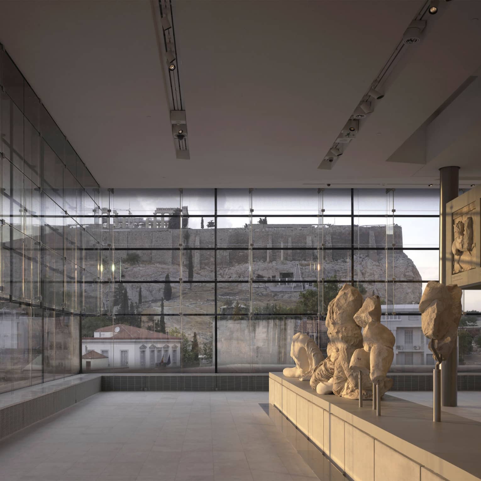 Greek sculptures on display in glass room overlooking ruins at Acropolis Museum