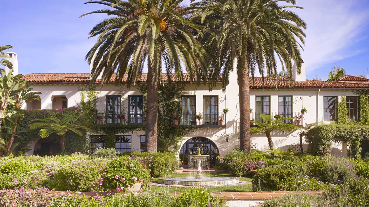 Fountain under palm trees in sunny garden in front of Four Seasons Hotel villa-style building