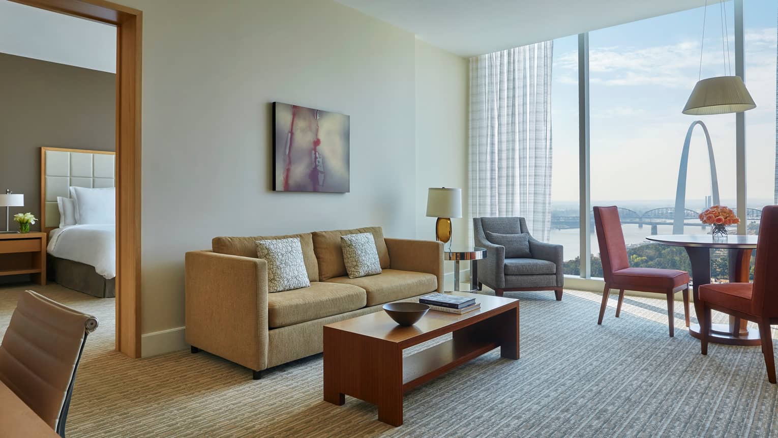 Arch one-bedroom suite living room with gold sofa, grey armchair and dining table, near separate bedroom