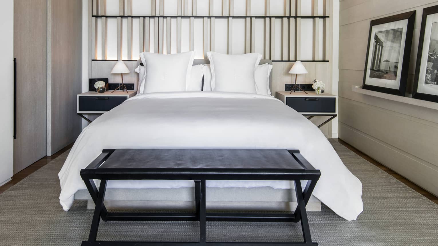 Bed with white sheets, black bench, two night stands, two framed photos