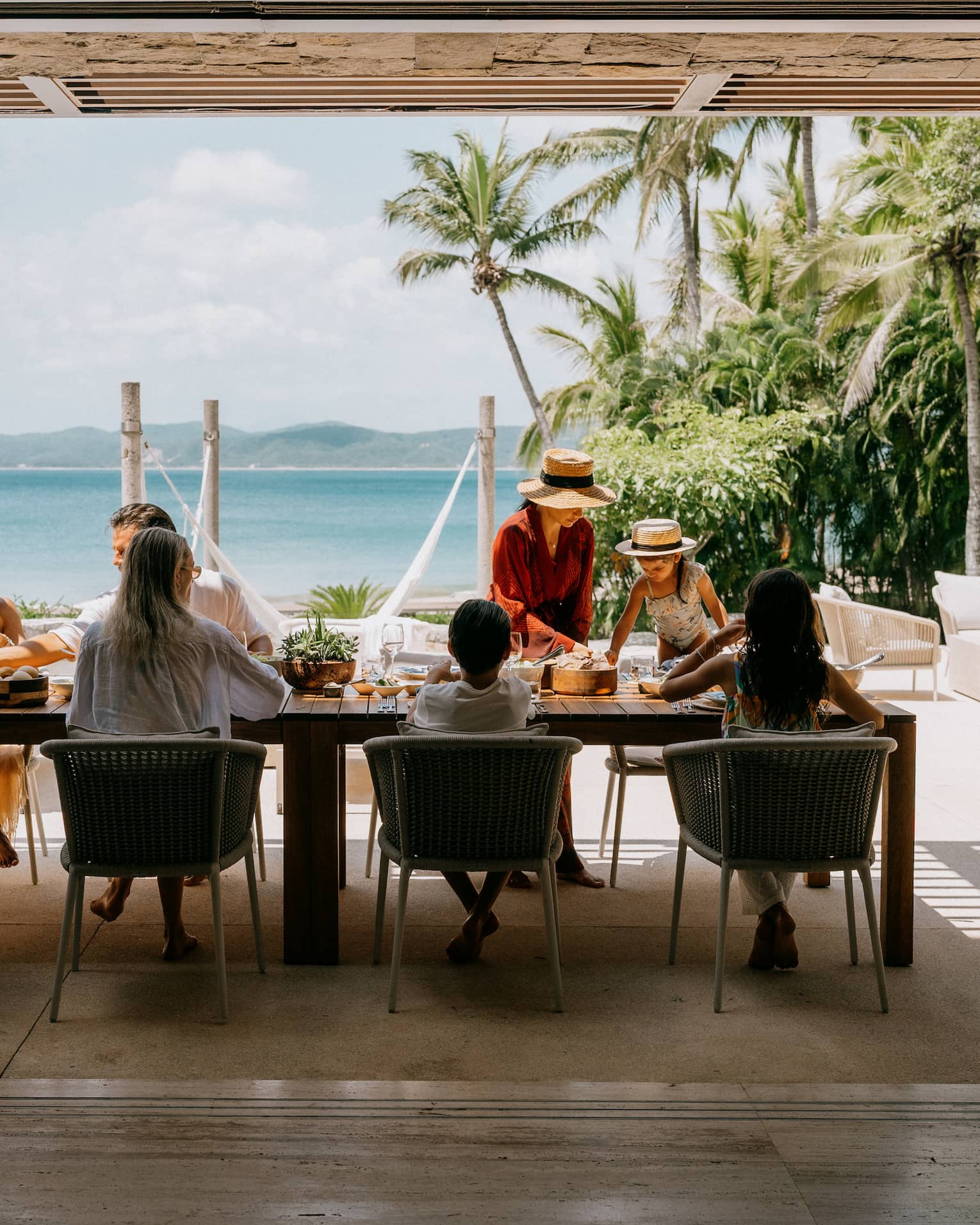 A group of people enjoy a meal in an outdoor dining setting looking out over the beach and ocean.
