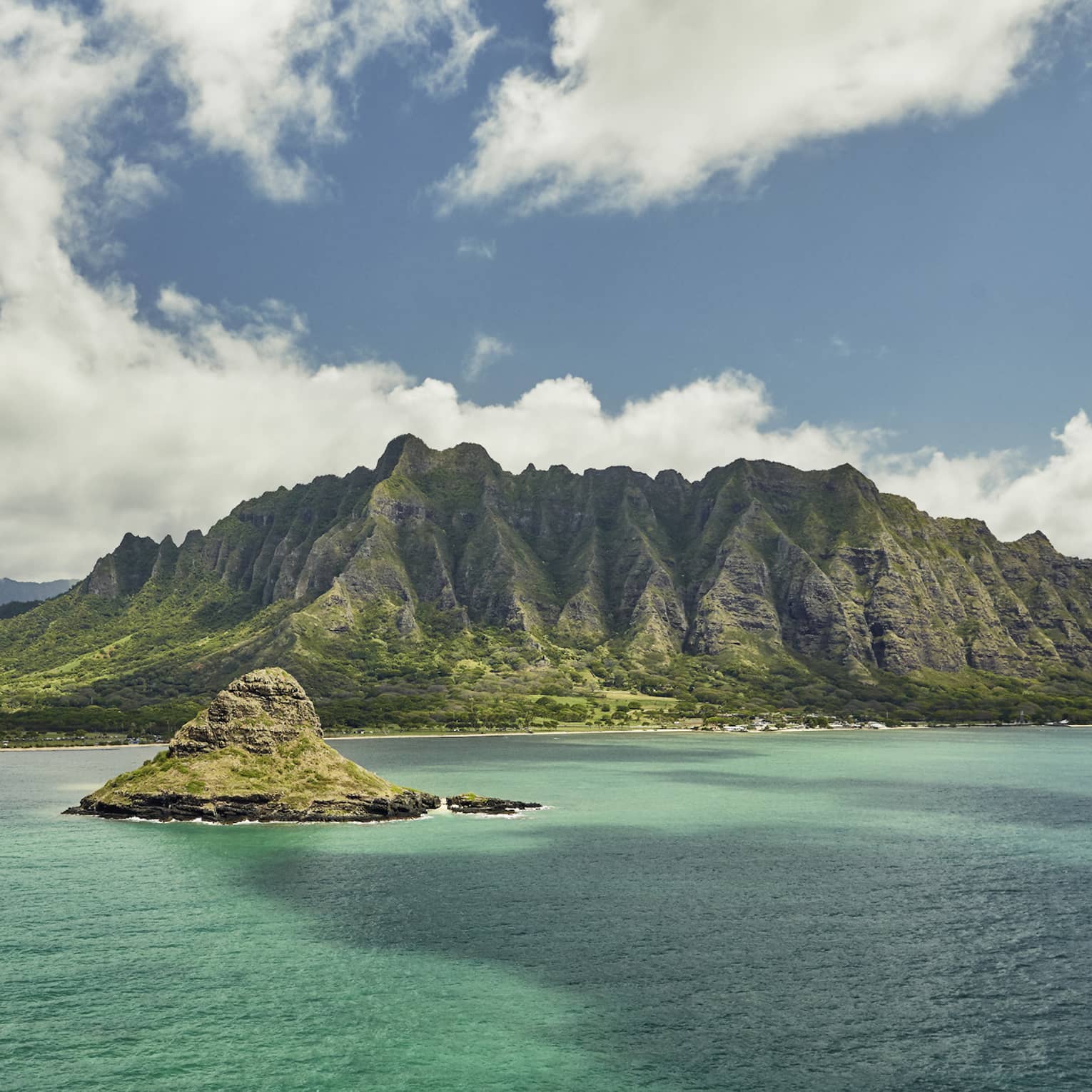 Sweeping green Oahu, Hawaii mountains, small island over turquoise lagoon, white clouds