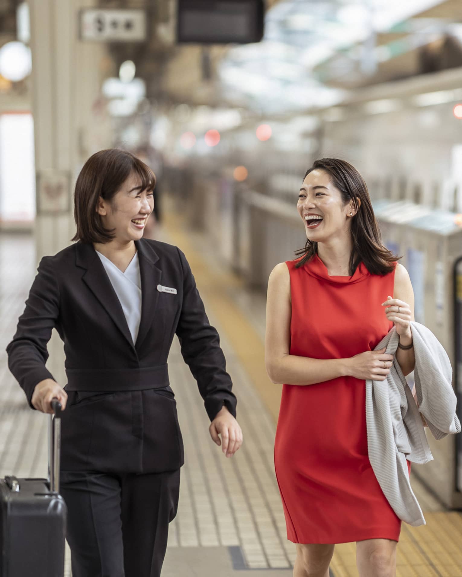 A Four Seasons employee holds a traveller's suitcase; laughing, they walk along the platform beside an N700 high-speed train.