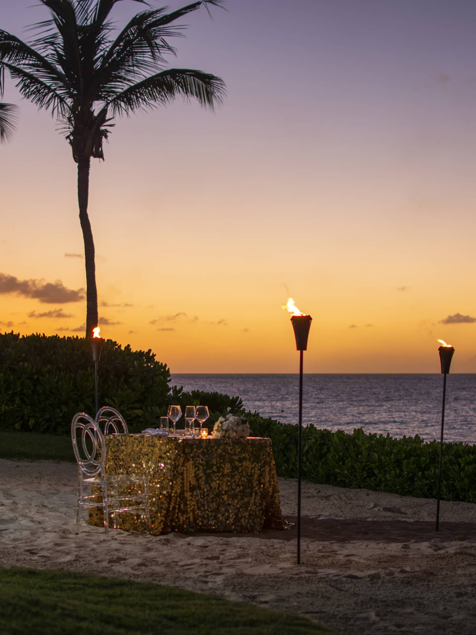 Romantic beachfront dinner setup with tiki torches and a sunset ocean view.